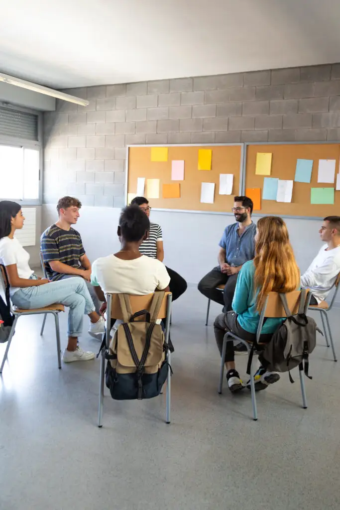 Unmasking Imposter Syndrome: Personal Stories and the Science Behind the Struggles high school students sitting in a circle sharing problems with classmates and teacher. support group. vertical image.